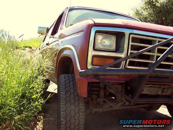 Low-angle front view of a red Ford Bronco with black tube bumper and off-road tire on a dirt trail