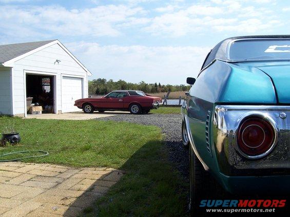red coupe parked outside garage, blue car in foreground