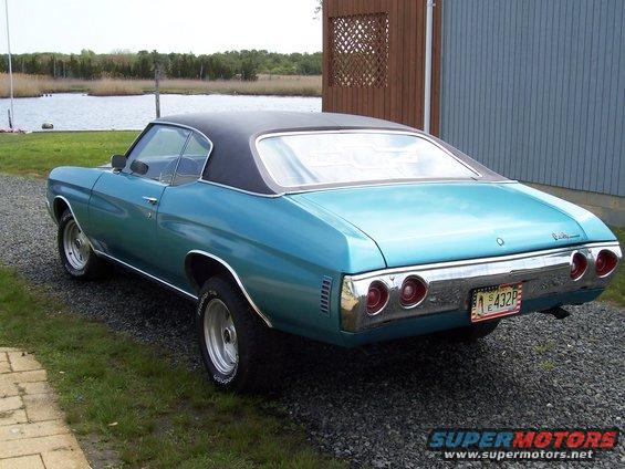 Blue 1970 Chevrolet Chevelle with black vinyl top parked on gravel near a building and water