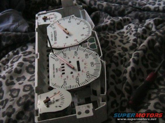 Car dashboard gauges with tachometer, speedometer, and fuel gauge. A screwdriver is visible to the right