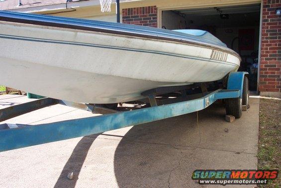 Boat on a trailer in front of a garage. Blue trim on boat, blue trailer