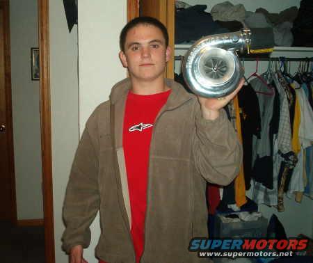 Man holding a silver turbocharger in front of a closet with clothes
