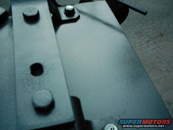 Close-up of metal brackets and bolts, with a SUPERMOTORS watermark at the bottom right