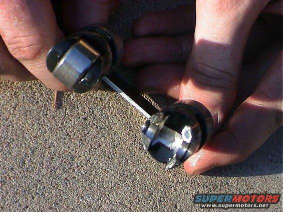 Hands holding two engine valve lifters, one with visible wear