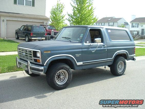 1982 Ford Bronco parked on street, another SUV and red vehicle in driveway behind it