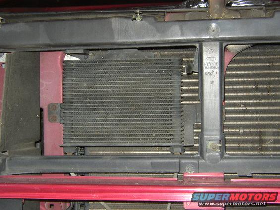 Close-up of a vehicle's front radiator and transmission cooler assembly. Red body panels are visible