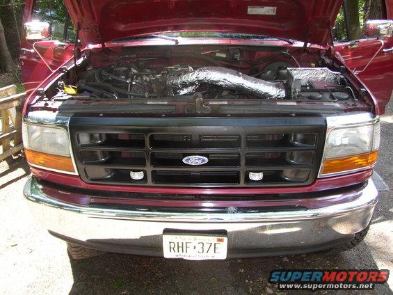 Front of a 1995 Ford Bronco with hood open, showing engine and black grille with Ford logo