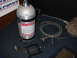 1985 Ford Crown Victoria LTD - Compucar nitrous oxide system components including a large tank, coiled hose, and fuel rail adapter are laid out on a carpeted surface.