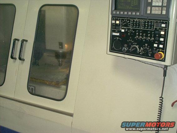 Control panel with buttons and dials mounted on a wall next to a machine with a window