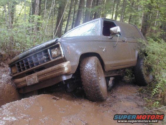 Mud-covered SUV stuck in a muddy ditch, front grille visible, tires deep in mud