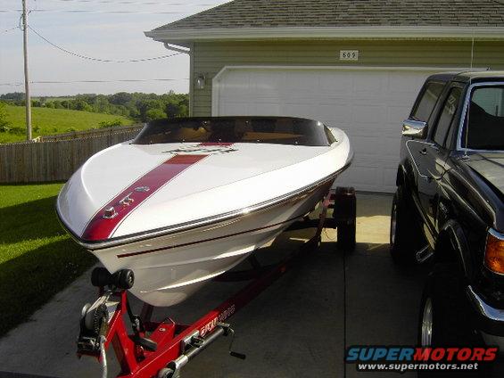 White boat with red stripe on trailer next to a black pickup truck in front of a garage