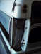 1994 Ford C-350 (Centurion Conversions) - The rear corner of a white truck shows rust and damage around the tailgate hinge area.