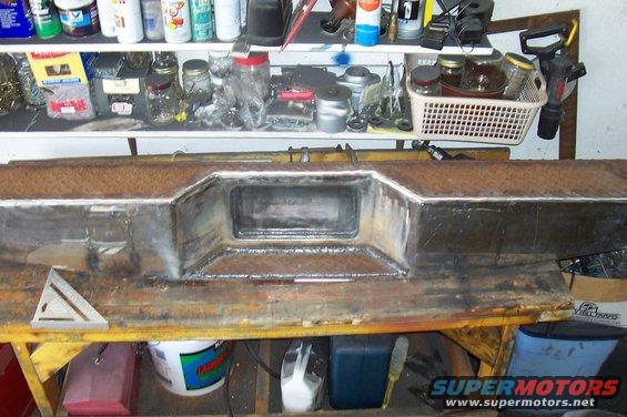 Custom metal bumper with a central rectangular cutout, resting on a workbench with tools and supplies in the background