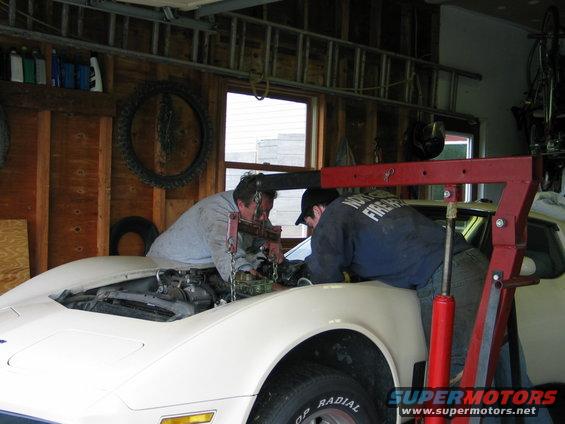 1981 Chevrolet Corvette with hood open, two mechanics working on engine using an engine hoist
