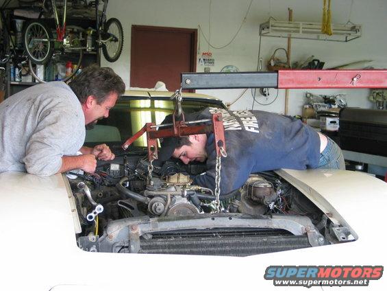 two guys working on car engine with hoist