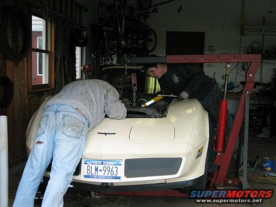 Cream-colored 1981 Chevrolet Corvette in a garage with two men working on the engine