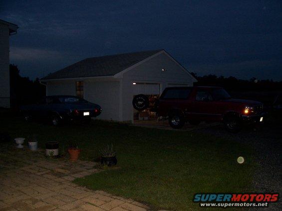 Dark blue car and red SUV parked in front of a garage at dusk