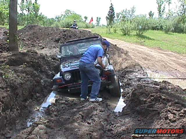 Jeep Wrangler stuck in a mud pit, front-left wheel submerged