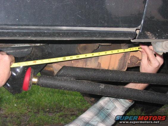 Measuring a black suspension component with a yellow tape measure