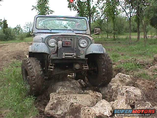 Jeep CJ-7 with large tires driving over rocks on a dirt trail