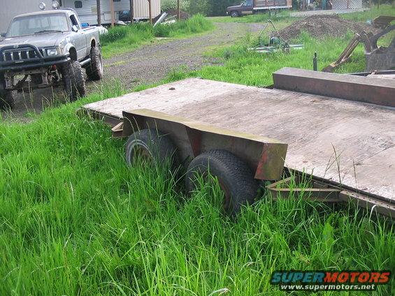 Lifted pickup truck parked next to a flatbed trailer in tall grass