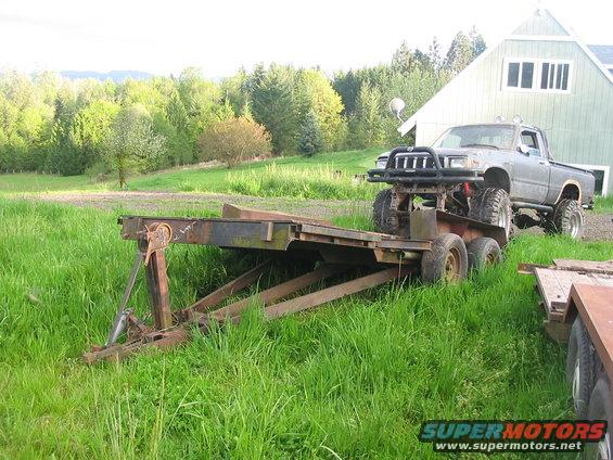 Gray pickup truck with off-road modifications on a rusty trailer in a grassy field