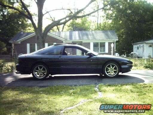 Side view of a black 1995 Ford Probe parked in a driveway with a house in the background