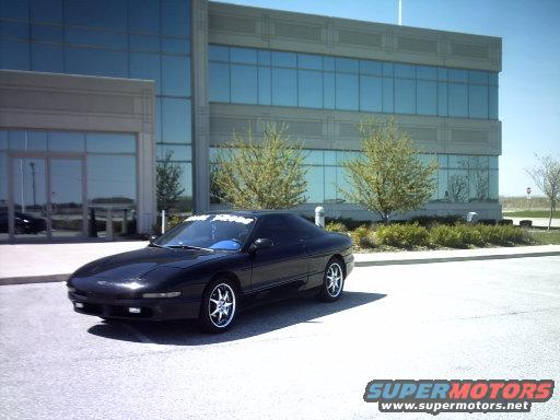 Black coupe parked in front of a modern office building, 3/4 front view