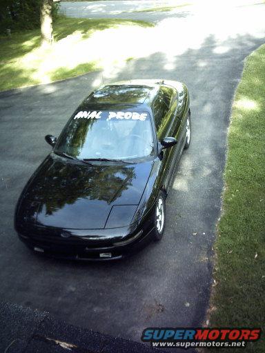 Black 1995 Ford Probe parked on asphalt driveway, custom banner on windshield reads 'ANAL PROBE'
