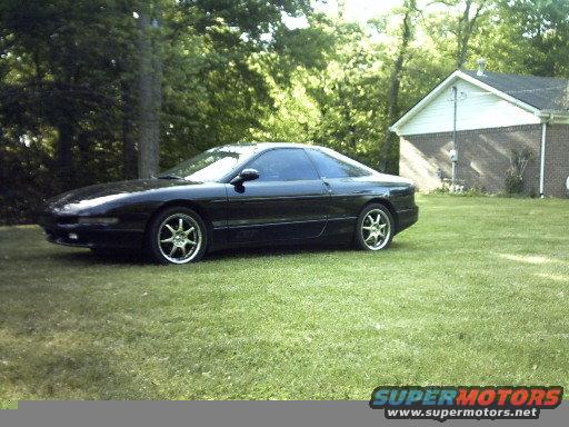 Black 1995 Ford Probe parked on grass, side view with front quarter visible. Aftermarket wheels. House and trees in background