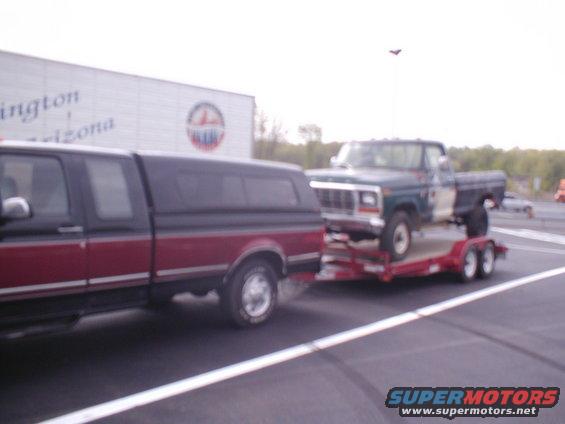 Green 1979 Ford F-Series pickup truck on a red trailer, towed by a red and black pickup truck