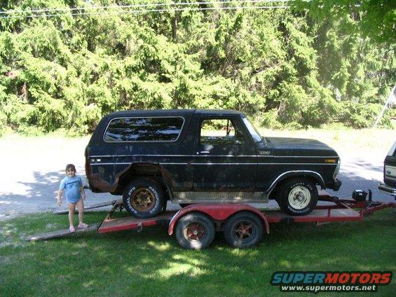 Black Ford Bronco on a red trailer, seen from the side with a child standing on the ramp
