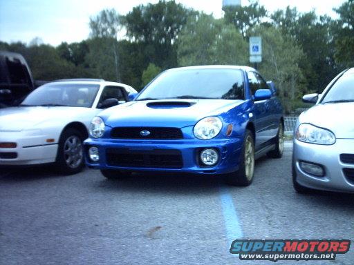 Blue Subaru Impreza WRX with gold wheels, front view, parked in a lot