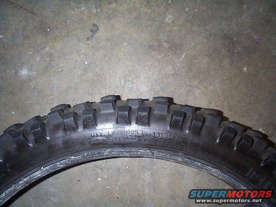 Motorcycle tire with knobby tread, showing sidewall markings for load and pressure