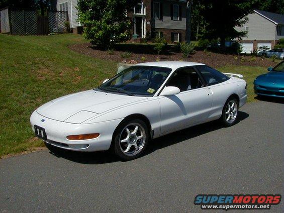 White Ford Probe parked on asphalt, 3/4 front view. Teal car visible in background