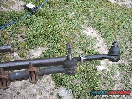 Tie rod ends and drag link assembly on grassy ground. One end is rusty with U-bolts