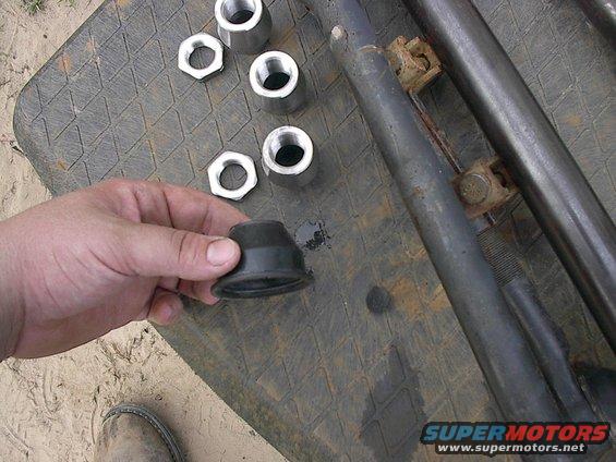 Hand holding black rubber bushing next to metal nuts and suspension components