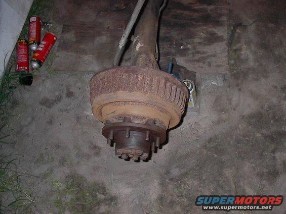 Rear axle assembly with drum brake, sitting on concrete. Three spray cans nearby