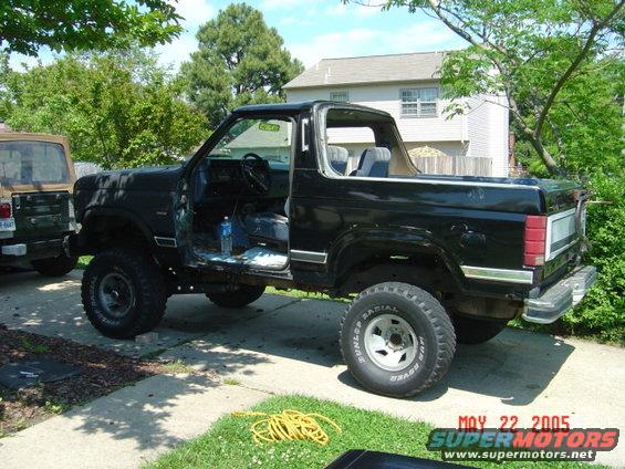 Black Ford Bronco, doors removed, parked next to a tan Jeep. The Bronco has aftermarket wheels and tires