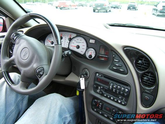 Driver's view of car interior, showing steering wheel, dashboard gauges, and radio. The car appears to be a Pontiac Grand Am