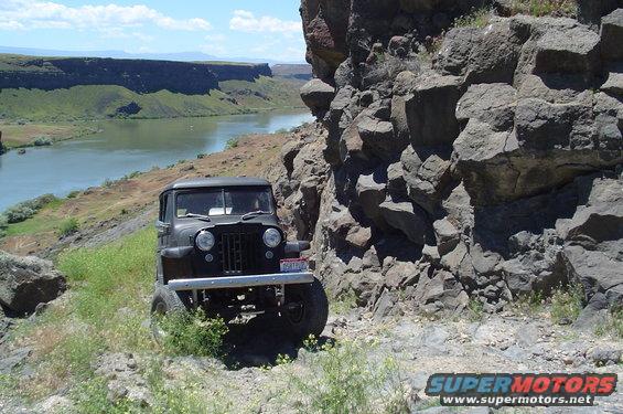 Black 1950s Jeep Willys parked on a rocky trail next to a river
