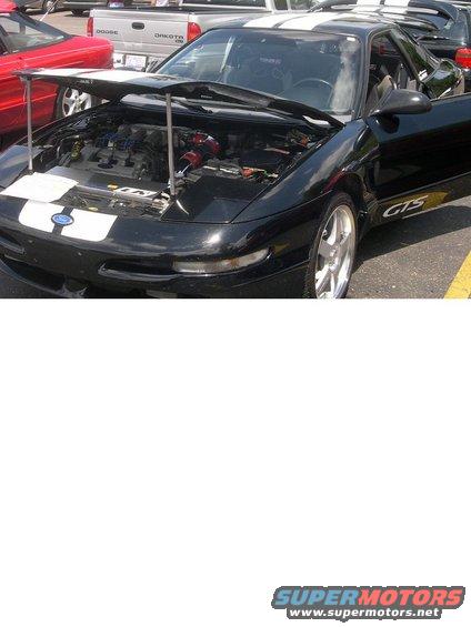 Black Ford Probe GTS with hood open, showing engine. White racing stripes on hood and roof. Other cars in background