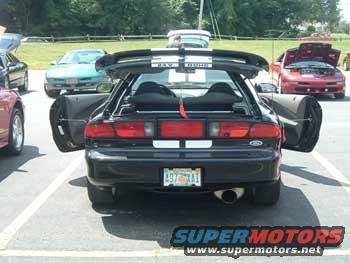 Rear view of black sports car with open doors and spoiler. Watermark 'SUPERMOTORS'