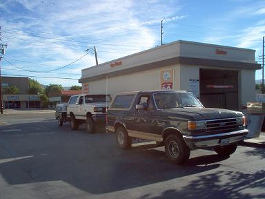 Dark 1987 Ford Bronco towing a trailer with a white Ford Bronco on it
