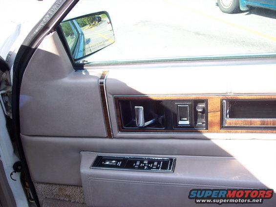 Car interior door panel with wood trim, chrome handle, and power window controls
