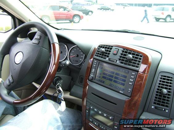 Car interior showing dashboard, steering wheel, and center console with navigation screen. Other vehicles visible through the windshield