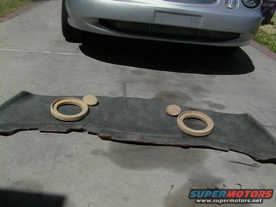 Silver car front with speaker mounts on a dark carpeted panel on the ground