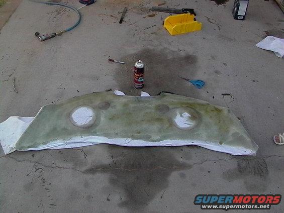 fiberglass part with two circular openings, resting on white cloth on concrete. Tools and spray can nearby
