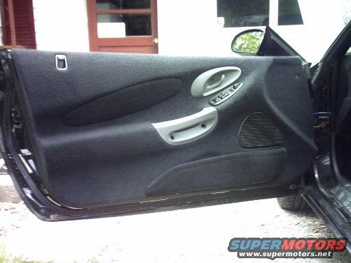 Black car door interior with gray handle and window controls, speaker grille visible