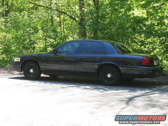 Black 2000 Ford Crown Victoria sedan parked on a paved surface with trees in the background